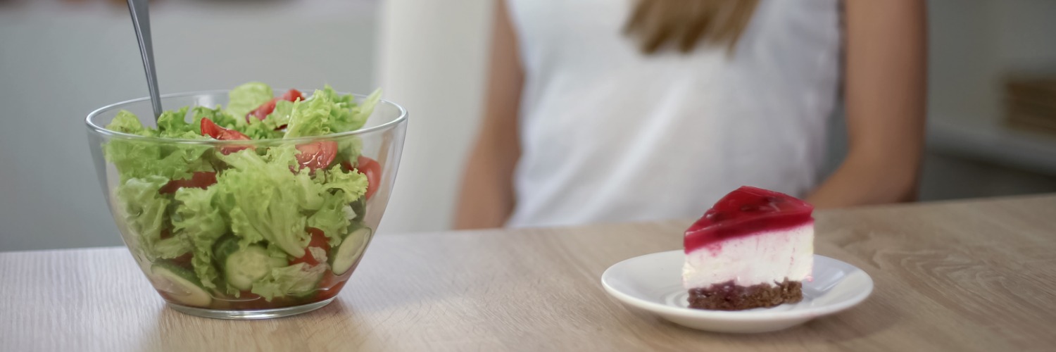 Junge Frau möchte Abnehmen durch Kalorienreduktion und hat die Wahl zwischen Salat und Torte.