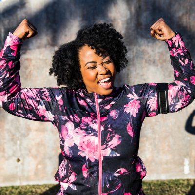 Frau zeigt lachend ihre Muskeln, einer der Energiespeicher während des Sport beim Intervallfasten