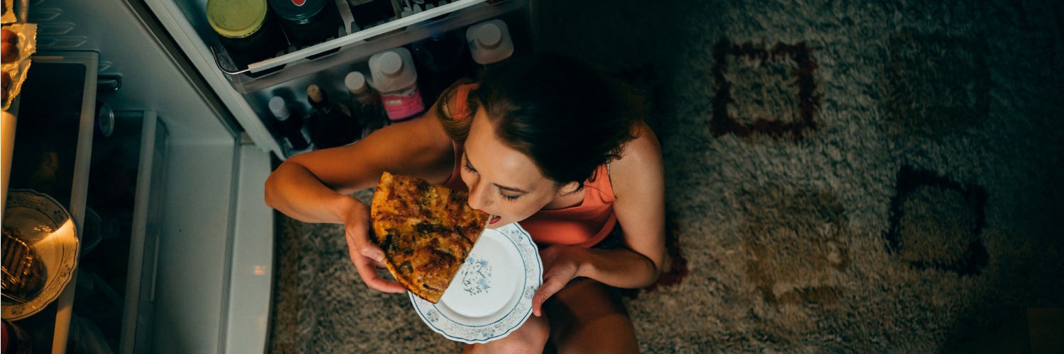 Hunger bei Keto: Frau isst vor dem Kühlschrank Pizza